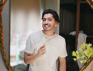 Man holding toothbrush and looking at his gums in mirror