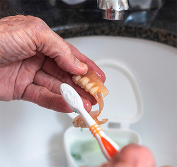 Person brushing their denture in a sink