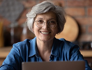 An older woman wearing glasses and showing off her new smile thanks to dental implants