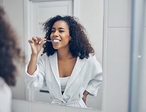 woman brushing her teeth in front of a mirror 