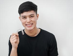 Young man holding Invisalign clear braces tray in Richardson