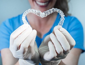 dental team member holding two Invisalign clear aligners in the shape of a heart 