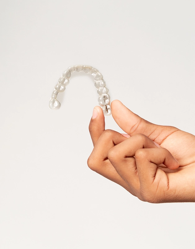 Hand holding a clear aligner against a white background
