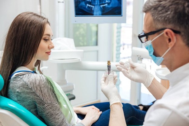 woman in dental chair looking at an implant model