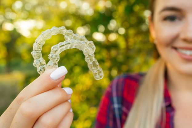 woman smiling holding Invisalign trays
