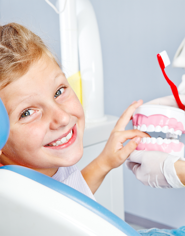 Child in the dental chair holding a large model of the teeth