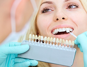 Dentist comparing woman's smile to porcelain veneer color options