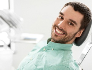 A young male patient wearing a green shirt and lying back in the dentist’s chair