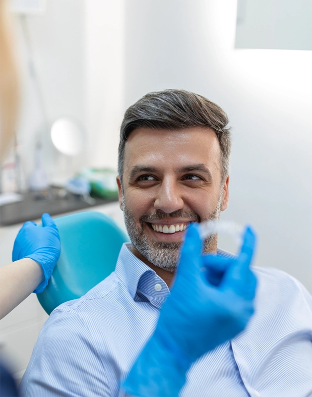 Man smiling as his dentist shows him a clear aligner