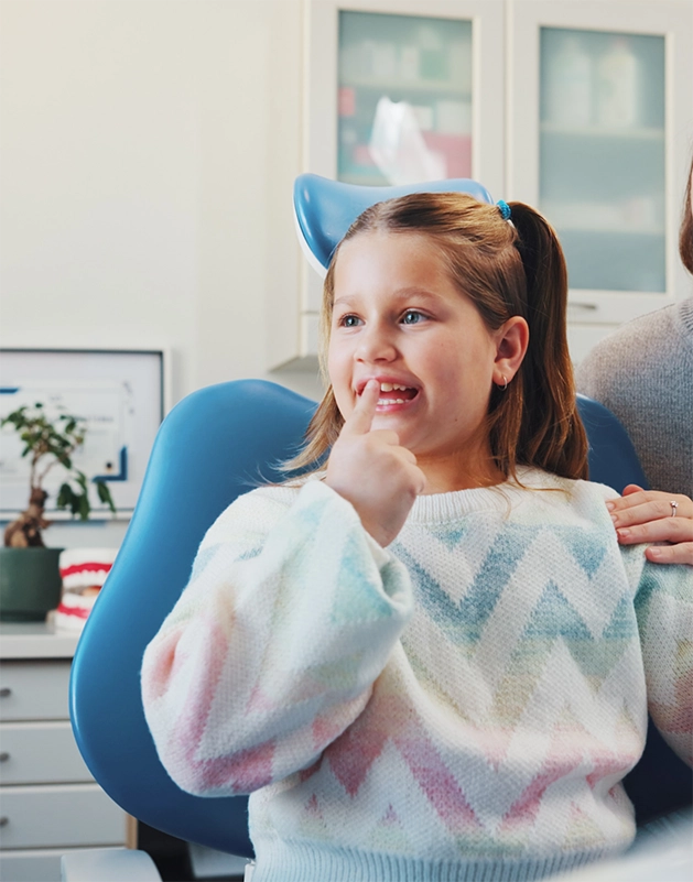 Child in the dental chair pointing to her smile