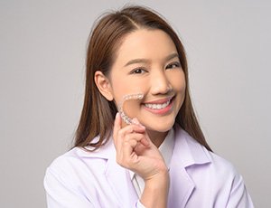 Happy woman holding SureSmile aligner close to her face
