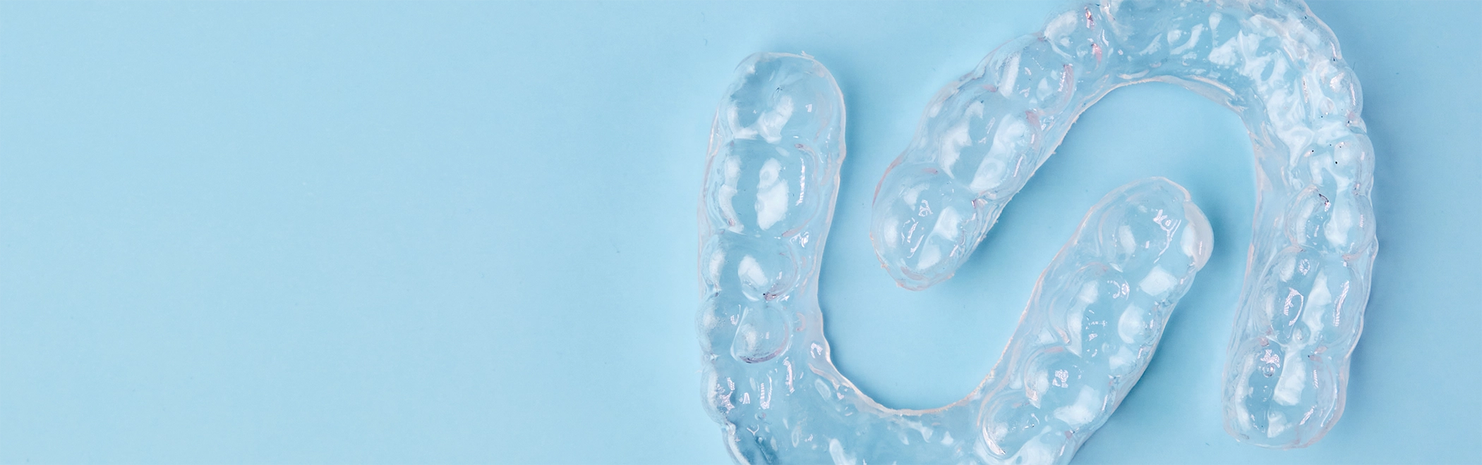 Two SureSmile aligners on a sky blue background