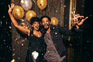 A smiling couple surrounded by gold confetti and balloons