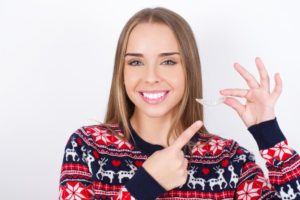 smiling woman holding a clear aligner for Invisalign in Richardson, TX