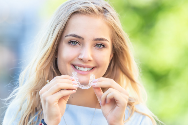 woman smiling holding invisalign aligner outdoors